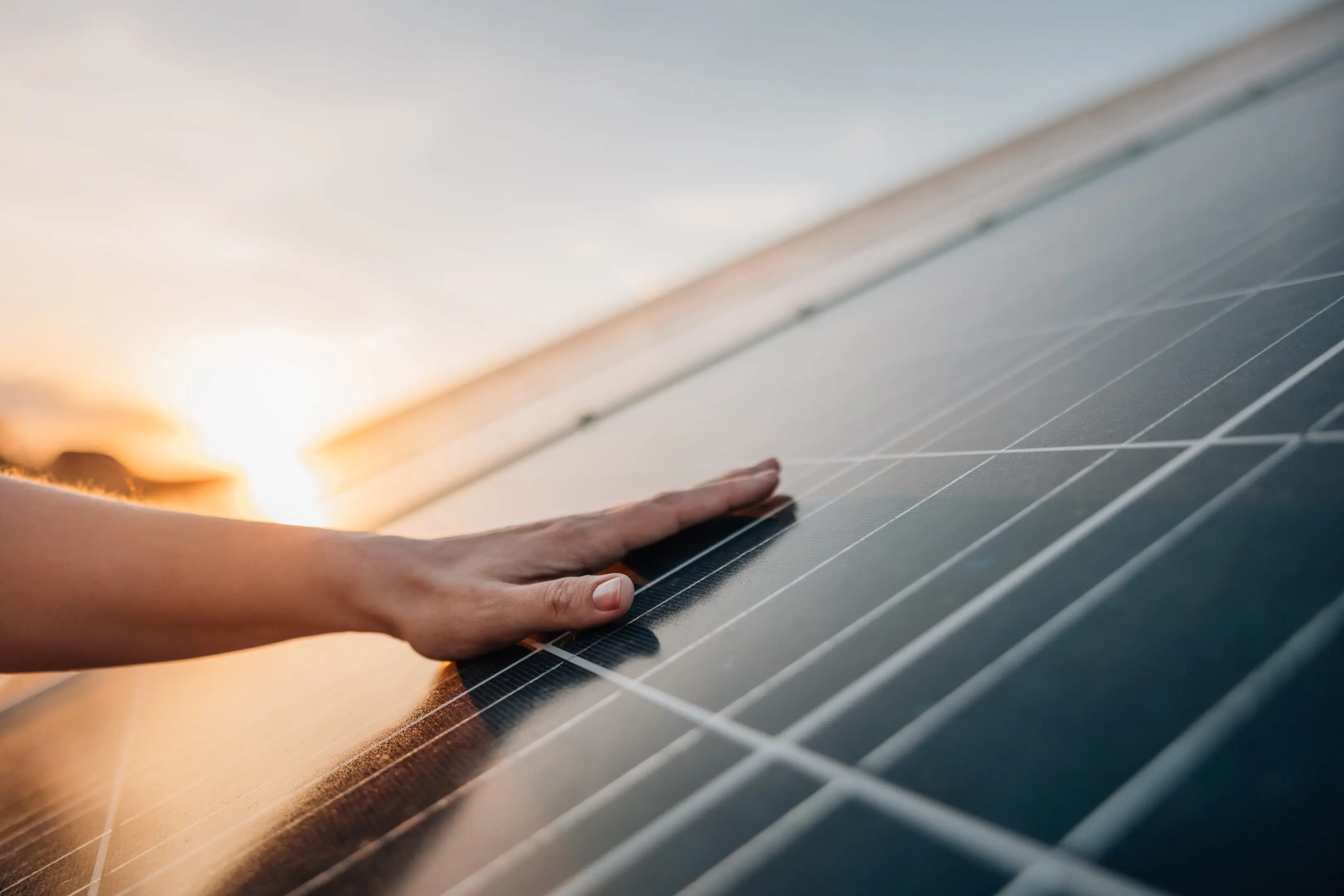 Hand touching solar panel at sunset.